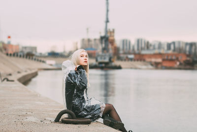 Young woman on river in city against sky