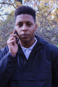 Portrait of young man talking on mobile phone while standing against trees