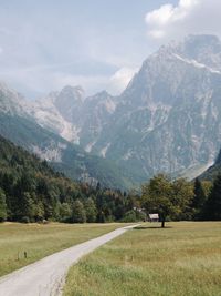 Road amidst field and mountains against sky