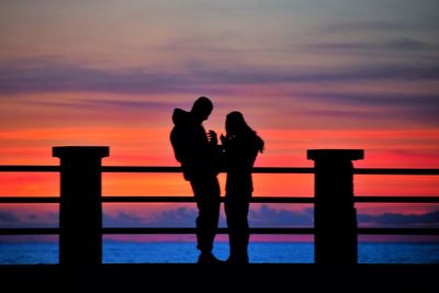 Silhouette women standing by railing against sky during sunset