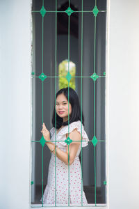 An asian woman in a white dress, she is looking at a camera standing behind green fence in temple 
