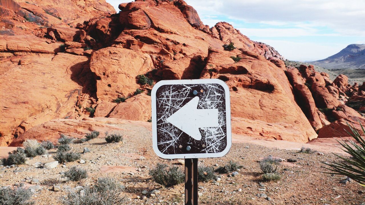 Arrow symbol on signboard against rocky mountains