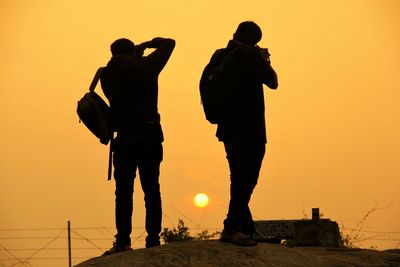 Silhouette men standing against orange sky