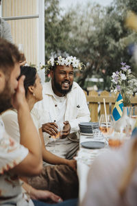 Smiling young man having fun with male and female friends during dinner party at cafe