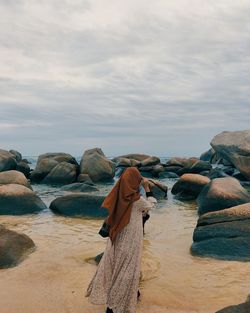 Rear view of man standing on rocks at beach against sky