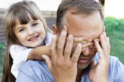 Little beautiful girl playing with her father in nature. a cheerful child covers the parent's eyes 