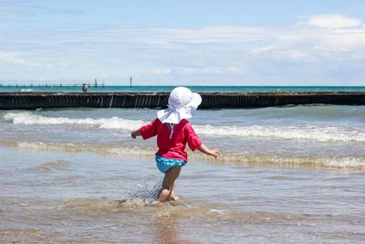 Rear view of child playing on shore against sky