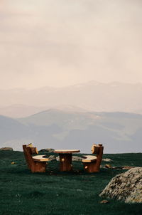 Empty benches and table on mountain against sky