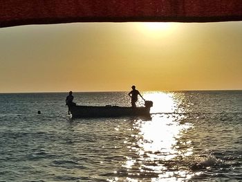 Silhouette people in sea against sky during sunset