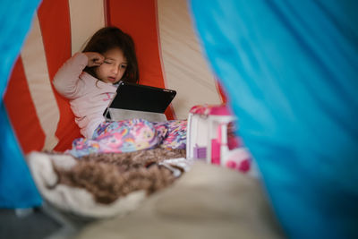 Four-year-old girl in pajamas looking at tablet in a little house