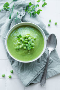 Fresh green pea soup bowl on white tile background