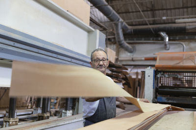 Man using wood laminating machine while standing in factory