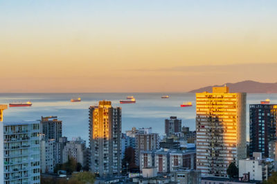 Sea by buildings against sky during sunset in city