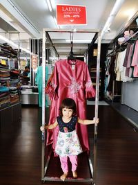Cute girl standing against dresses in store for sale 