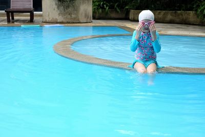 Girl wearing goggles while sitting in swimming pool