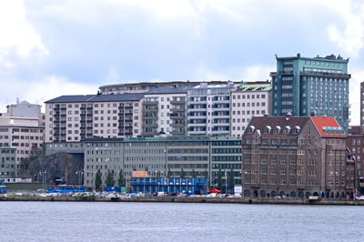 Buildings at waterfront against cloudy sky