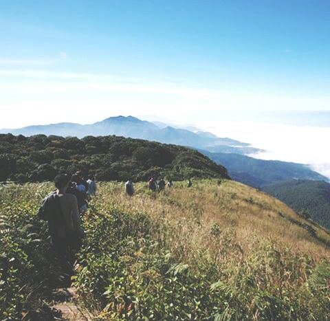 mountain, landscape, sky, tranquil scene, lifestyles, tranquility, men, leisure activity, scenics, mountain range, beauty in nature, rear view, nature, person, field, non-urban scene, standing, hiking