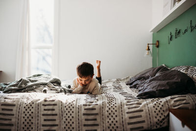 Young boy laying on bed watching on tablet in modern bedroom