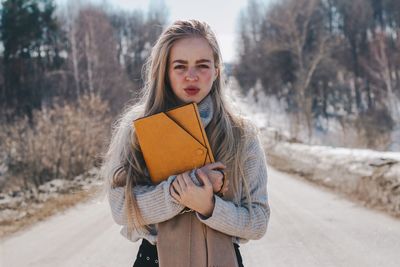 Portrait of beautiful young woman holding file while standing on road in winter