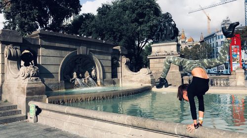 Woman doing handstand against fountain in city