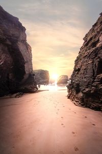 Rocks on beach against sky during sunset