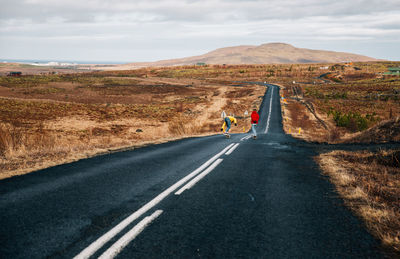 Full length of young man and woman skateboarding on road against landscape