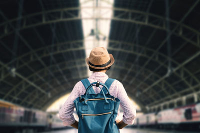 Rear view of man wearing hat and carrying backpack standing at railway station
