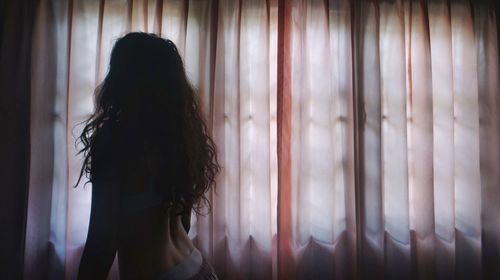 Silhouette of woman standing by curtains at home