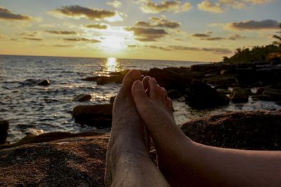 Low section of person on rock at beach during sunset