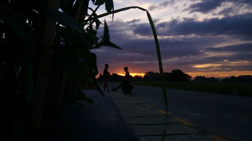 Silhouette men on road against sky during sunset