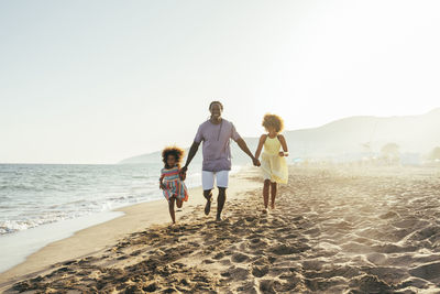 Playful man holding daughter's hands running at beach