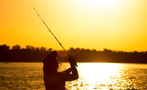 Silhouette man fishing at sunset