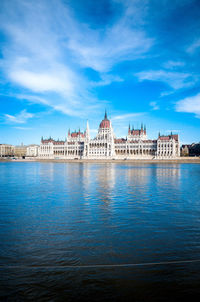 Hungarian parliament building by danube river against sky