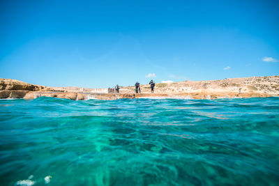 Mid distance view of scuba divers standing by sea against sky