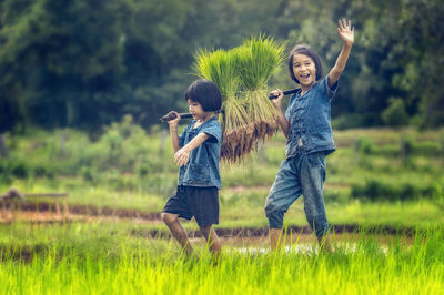 Full length of girls carrying rice crops while walking on field