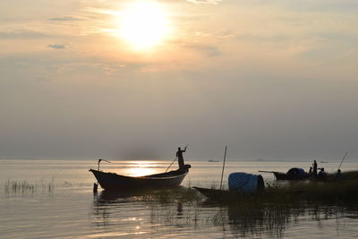 Men fishing on beach against sky during sunset