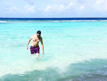 Shirtless man walking at beach against sky on sunny day