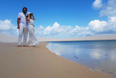 Couple standing at beach against cloudy sky