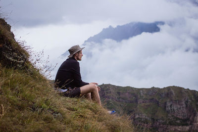 Thoughtful hiker sitting on grassy hill against cloudy sky