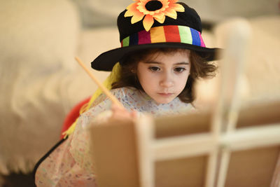 Cute girl wearing hat painting sitting at home