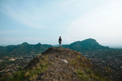 Rear view of man standing on rock against sky