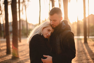 Young happy couple in love romancing while standing in park at sunset