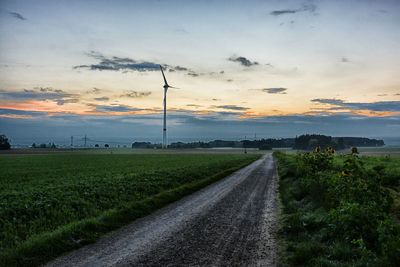 Road amidst field against sky during sunset