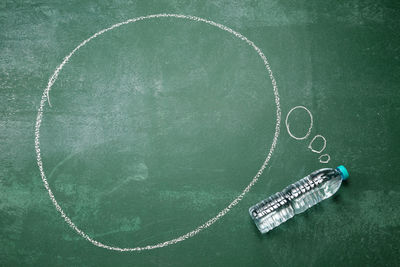 Directly above shot of blank speech bubble with water bottle on blackboard