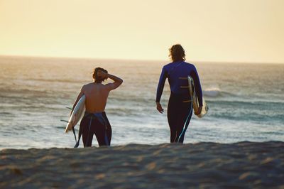 Rear view of male friends carrying surfboards at beach