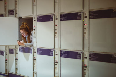 Young woman using phone in locker