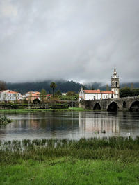 Arch bridge over river by buildings against sky