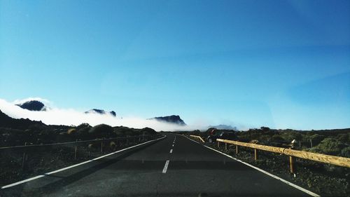 Road leading towards mountains against blue sky