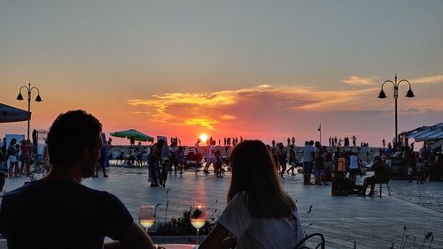 People by sea against sky during sunset