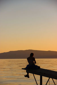 Silhouette man sitting in sea against clear sky